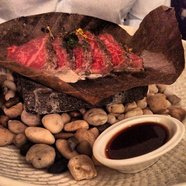 small, brown bowl of raw food sits atop a rock strewn dish with dipping sauce