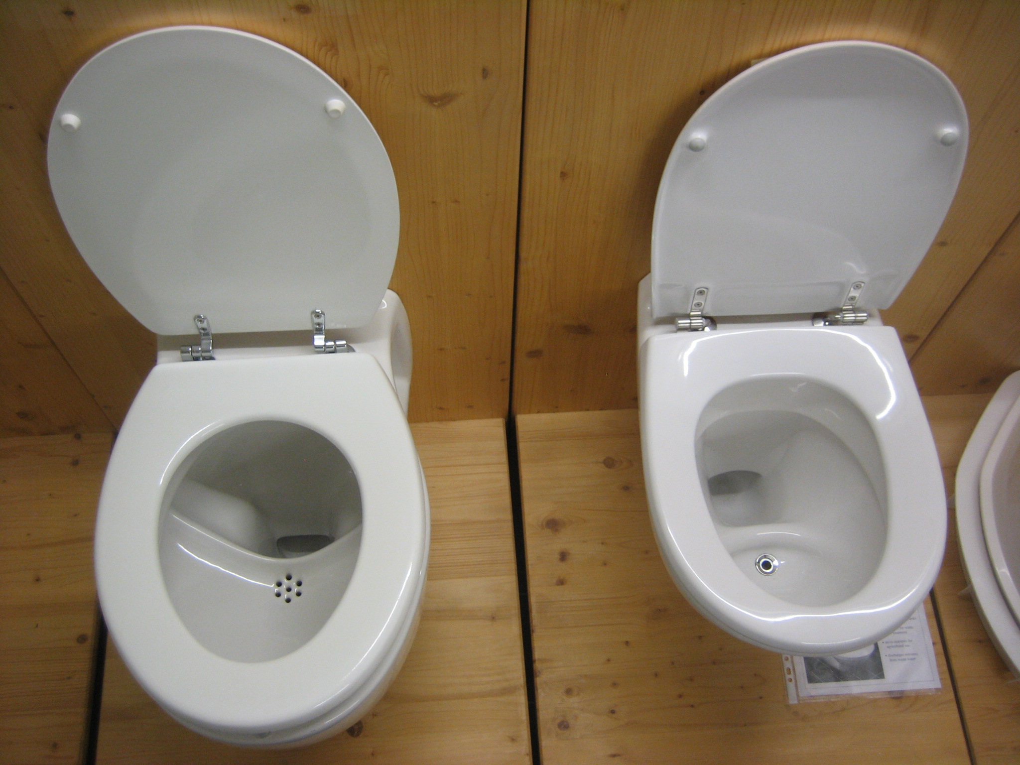 two toilets sitting on top of a wooden floor