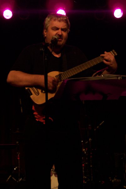 a man standing next to a microphone while playing a guitar