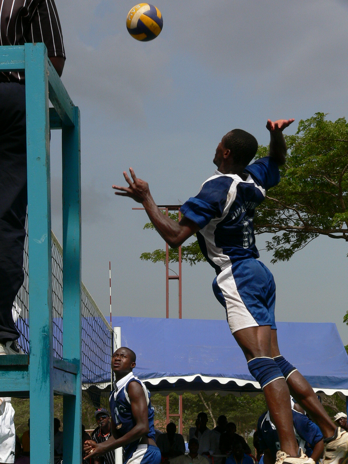 a man jumping to reach a yellow and blue volleyball