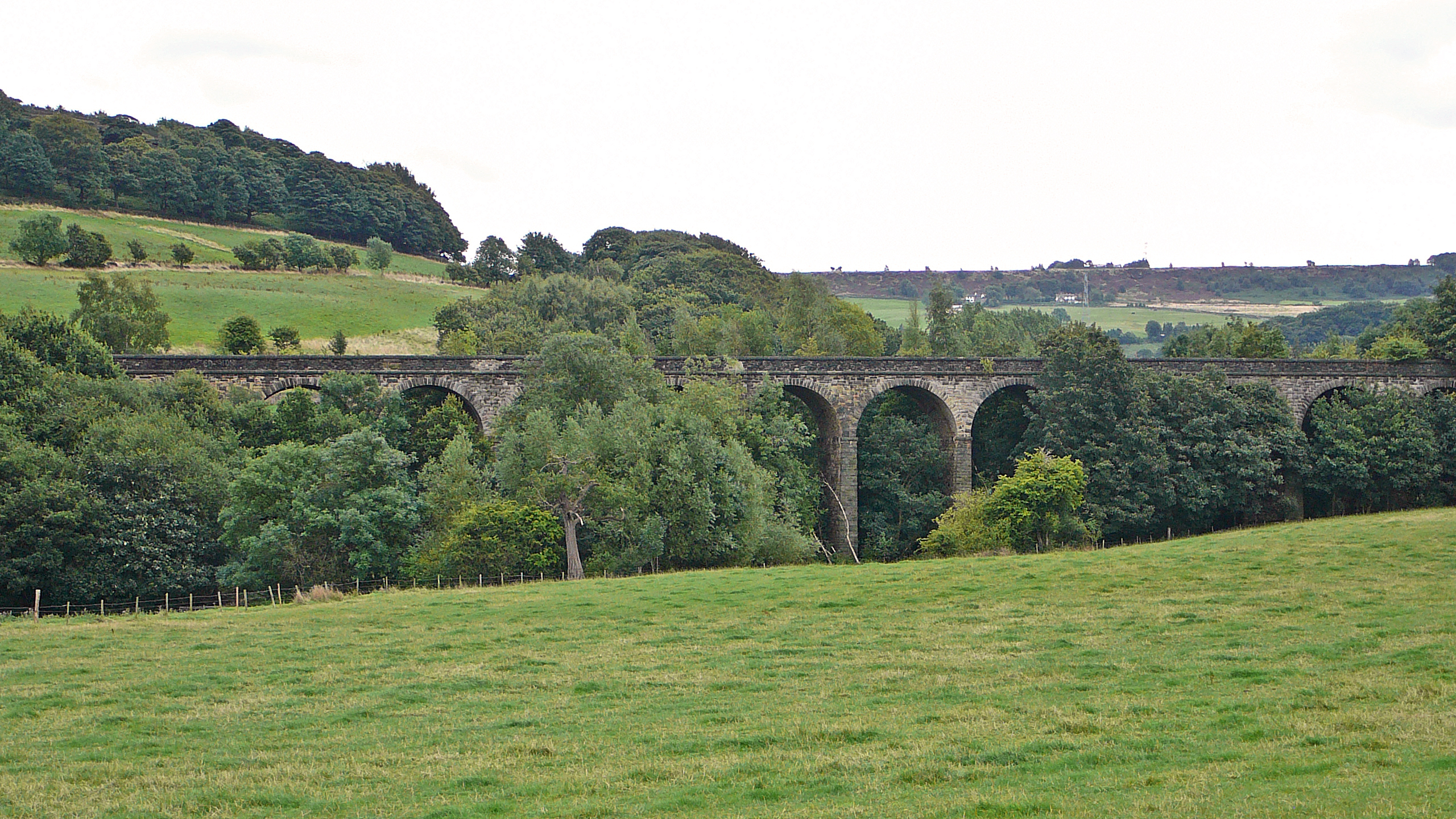 a green field with trees and a bridge in the background