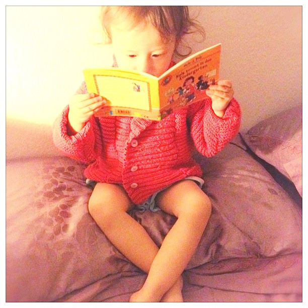 a girl sitting on top of a bed reading a book