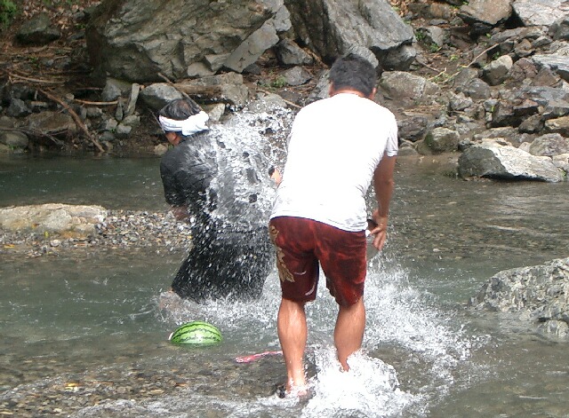 two guys standing in a stream playing with a ball