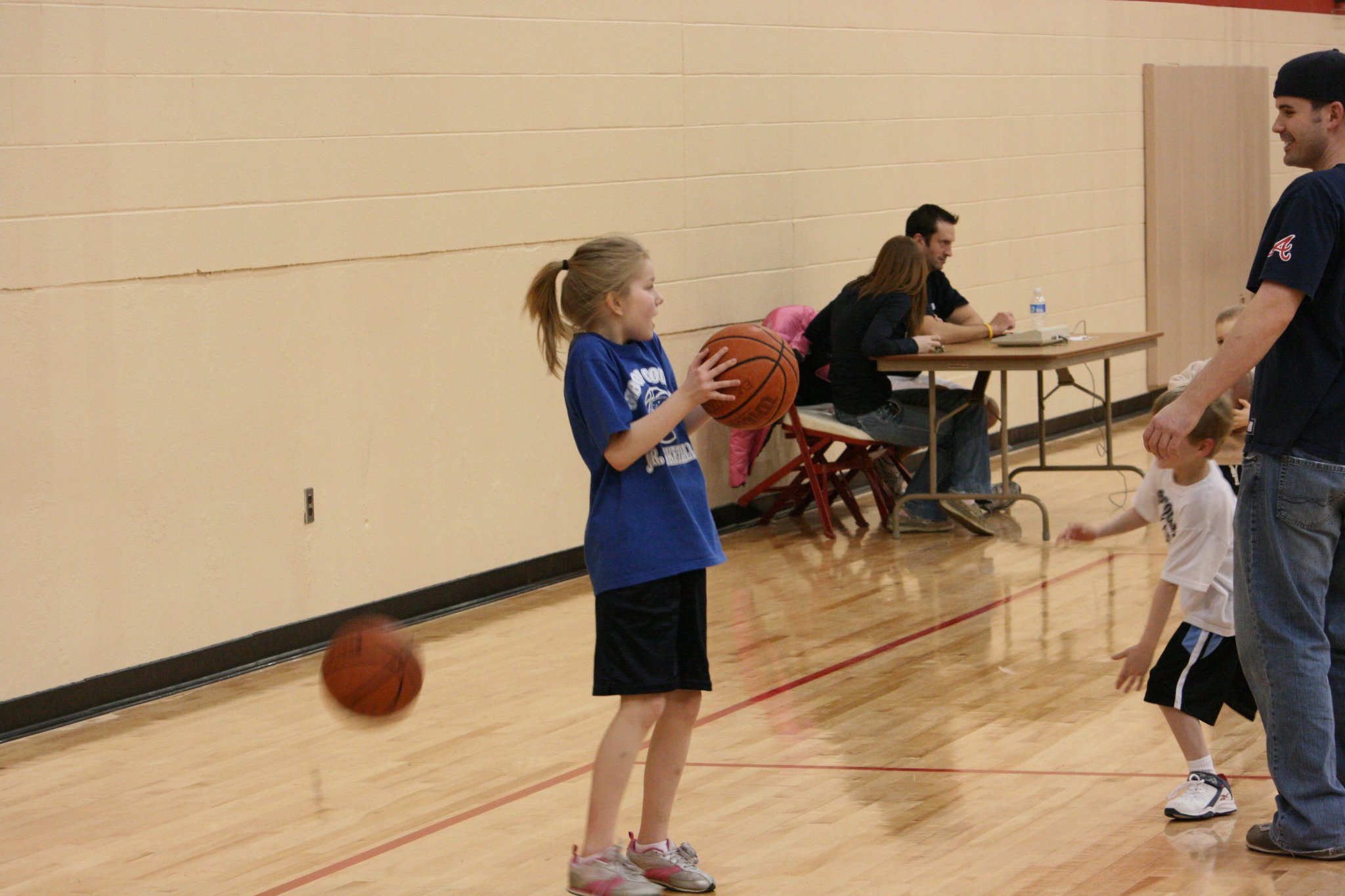 an adult teaches a young basketball player to toss the ball