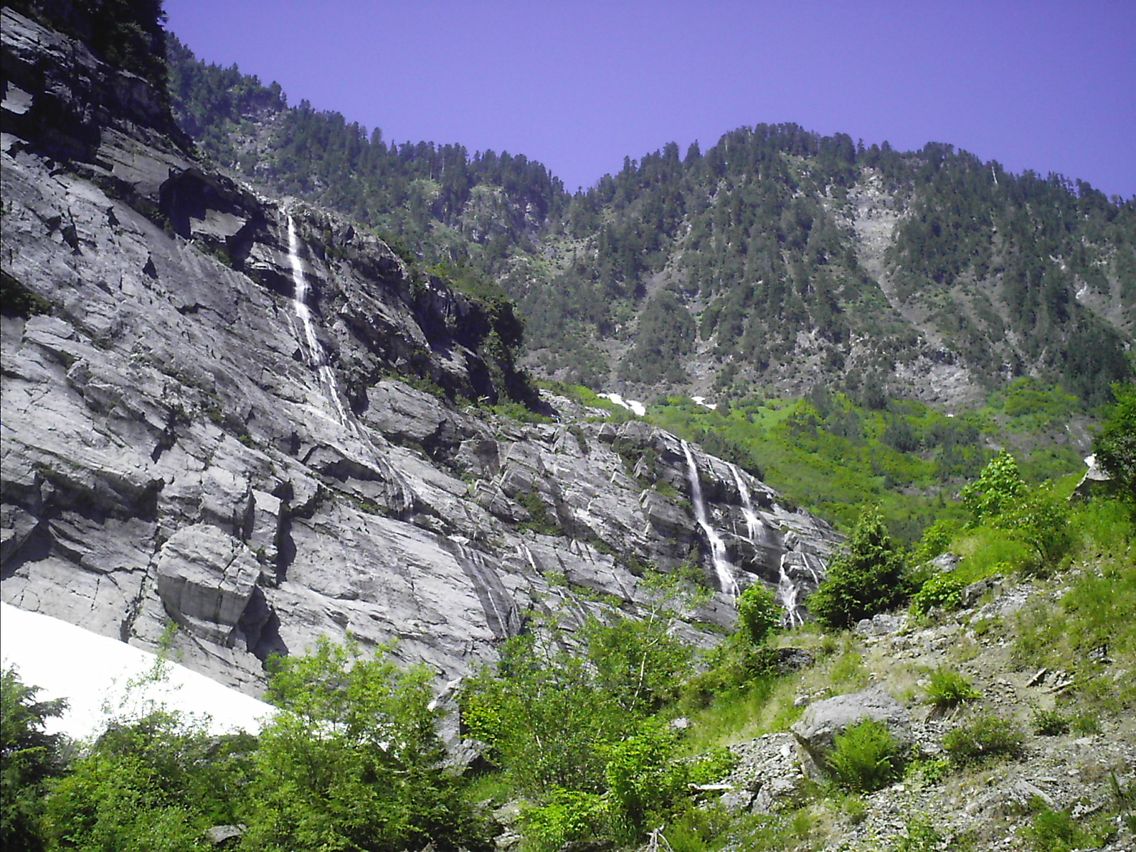 a waterfall on top of a large rock wall next to trees