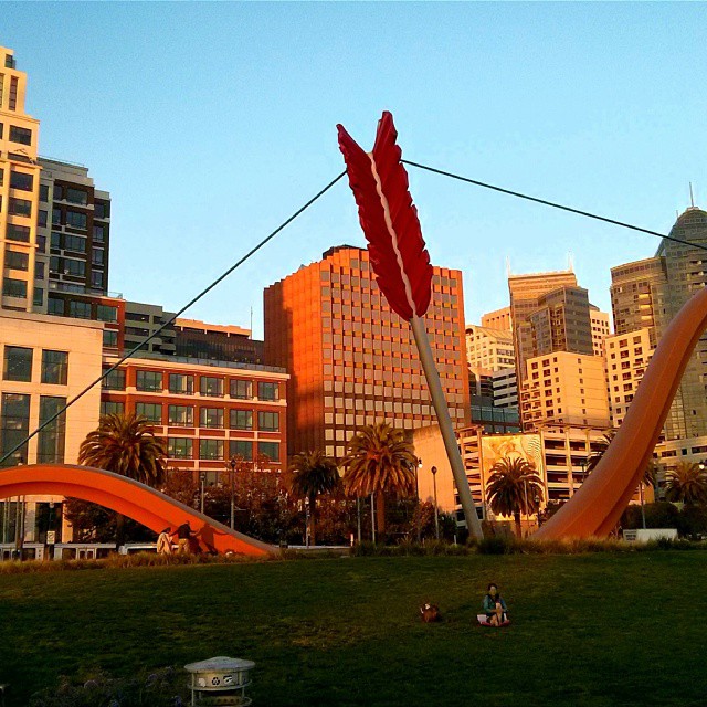 a sculpture in the grass in front of tall buildings
