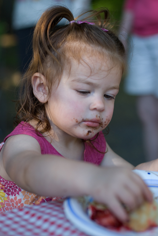 a small girl with sprinkled face and arms eating cake