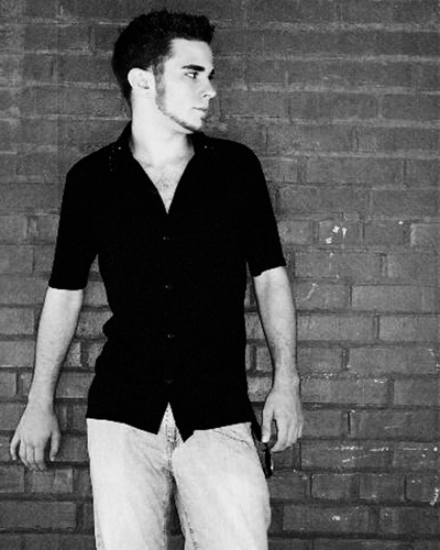 a man standing next to a wall while wearing jeans and a black shirt