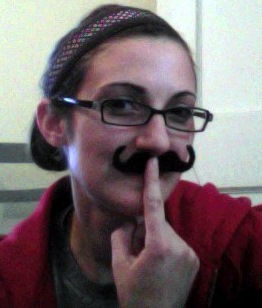 a woman with glasses and a fake moustache holds a finger up to her mouth