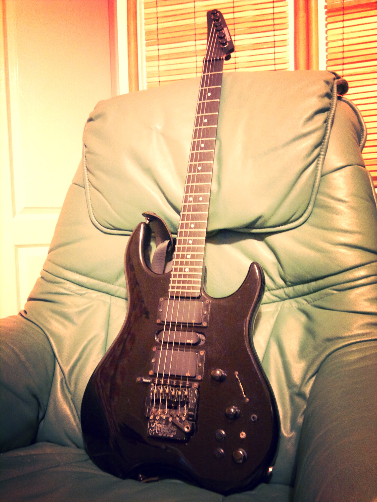a black guitar lying on a chair by a window