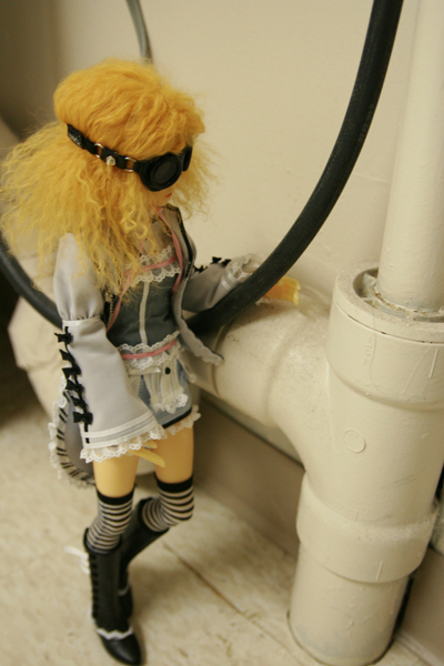 doll with large head dressed in costume and boots with a hair drier standing near pipes