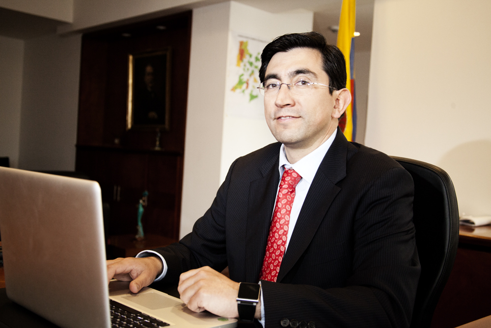 a man in a suit with glasses sits at a desk using his laptop computer