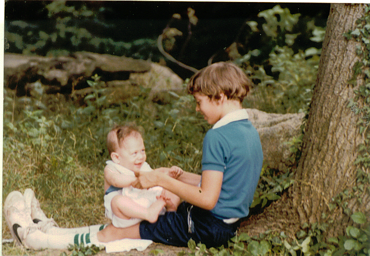 two s sit on the ground and talk with one of them holding a baby