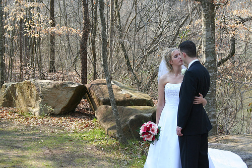 a man and woman in formal wear at a park with flowers on their bouquet
