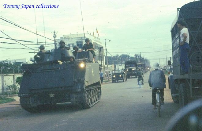 military vehicles moving down the street with people riding on them