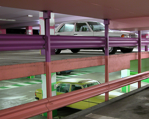 a yellow car and a pink truck are parked in a parking garage