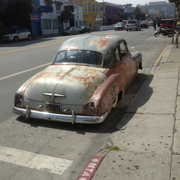 an old rusty car sitting on a street