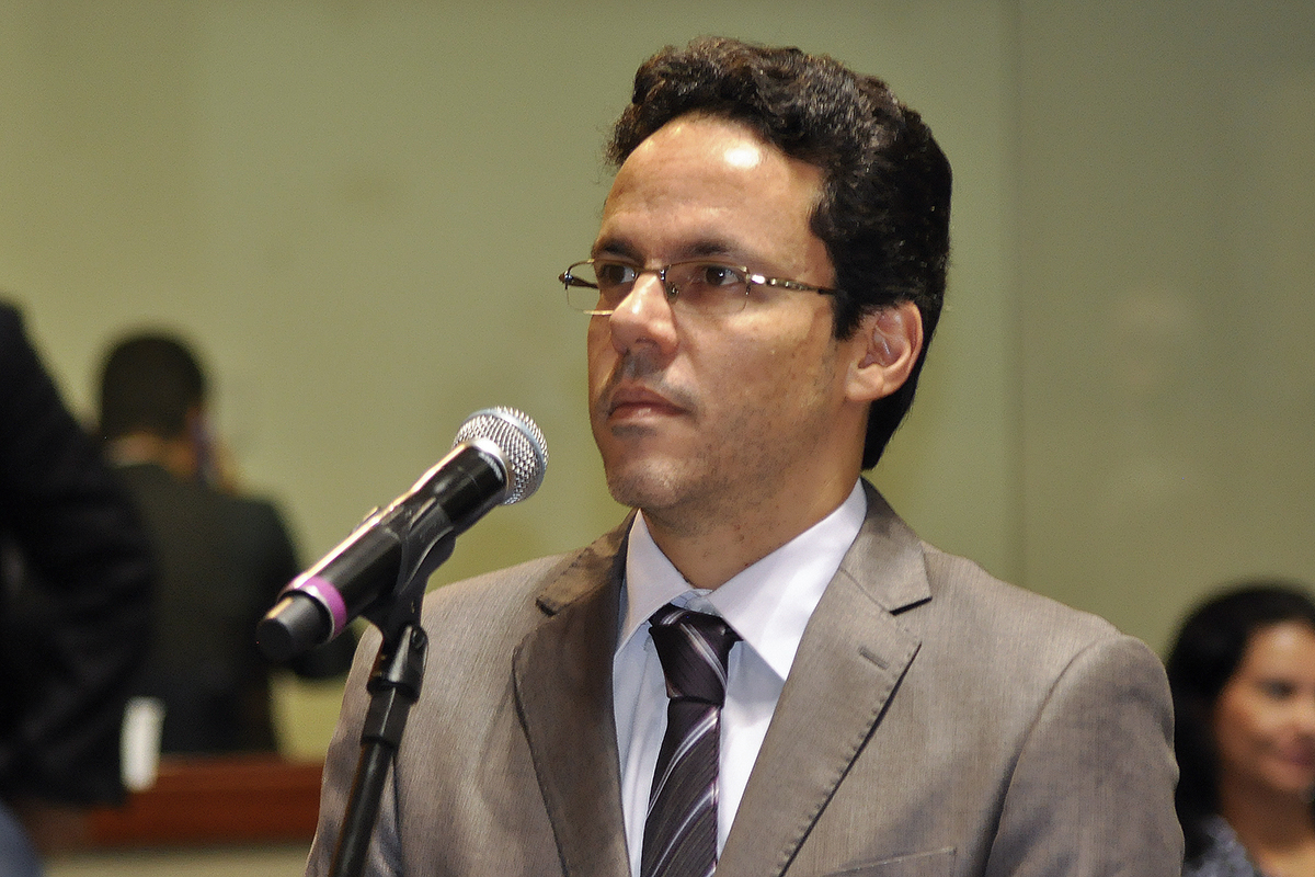 a man wearing glasses and a suit speaking into a microphone