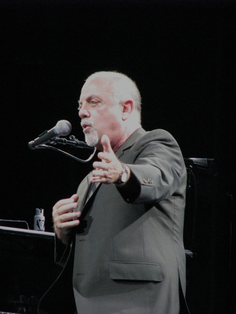 a man with a microphone standing in front of a piano