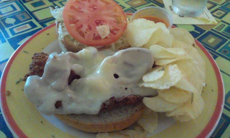 a hamburger topped with meat and sauce with potato chips