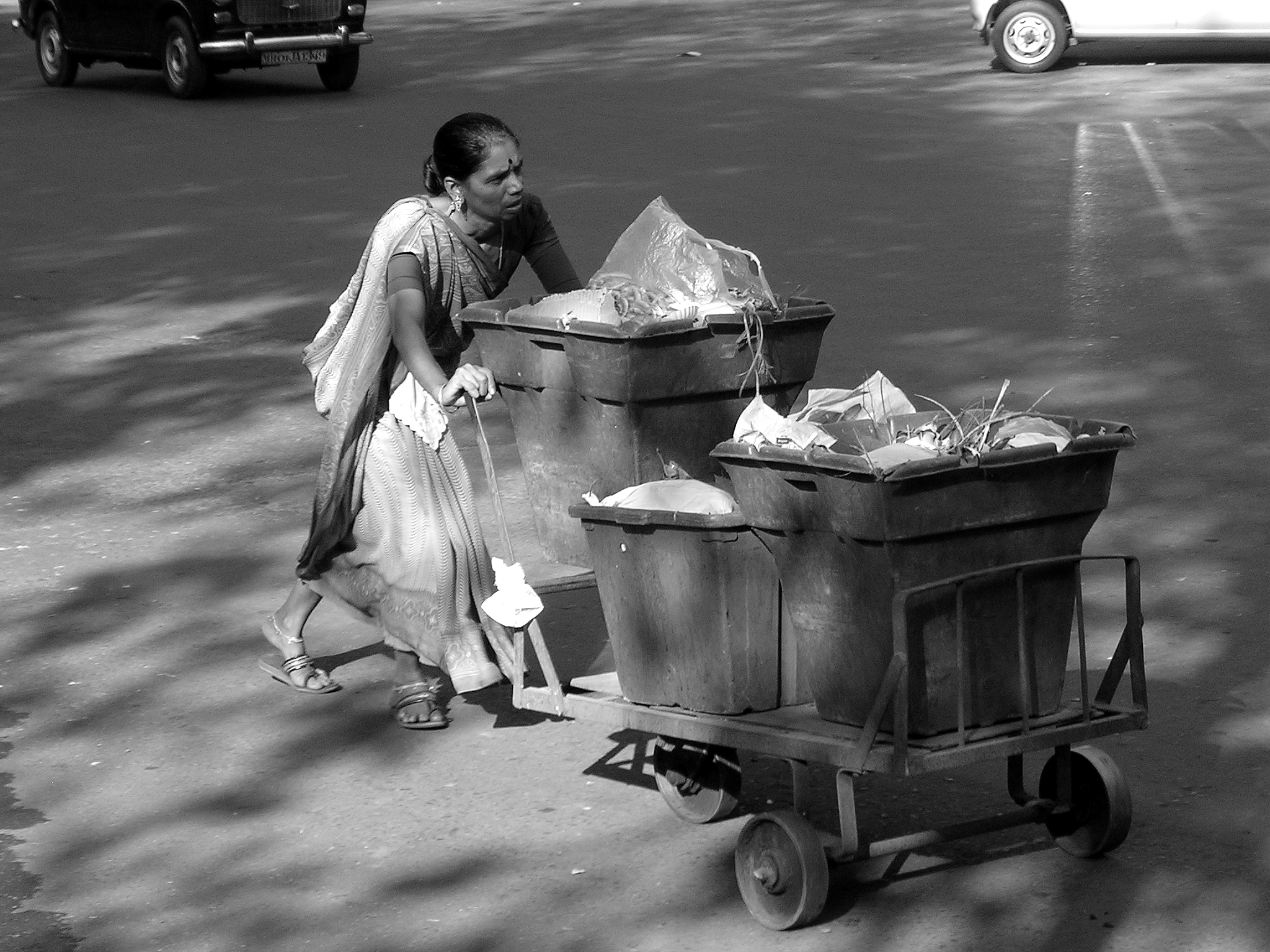 a woman walking behind a cart of trash