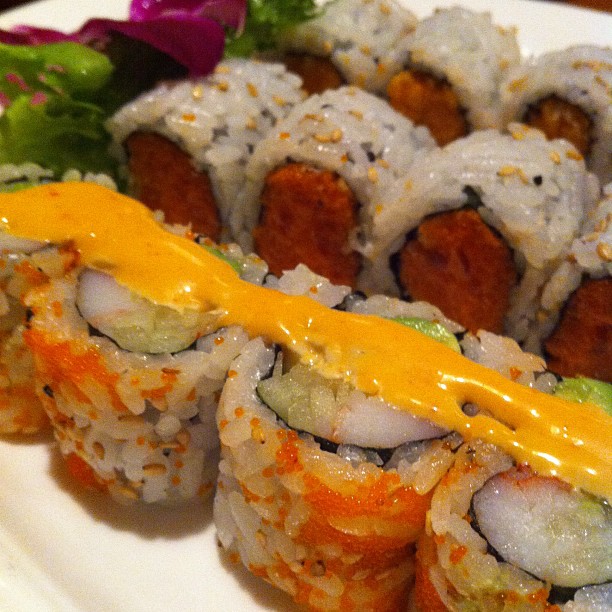 sushi rolls with orange sauce on white plate with red and purple salad