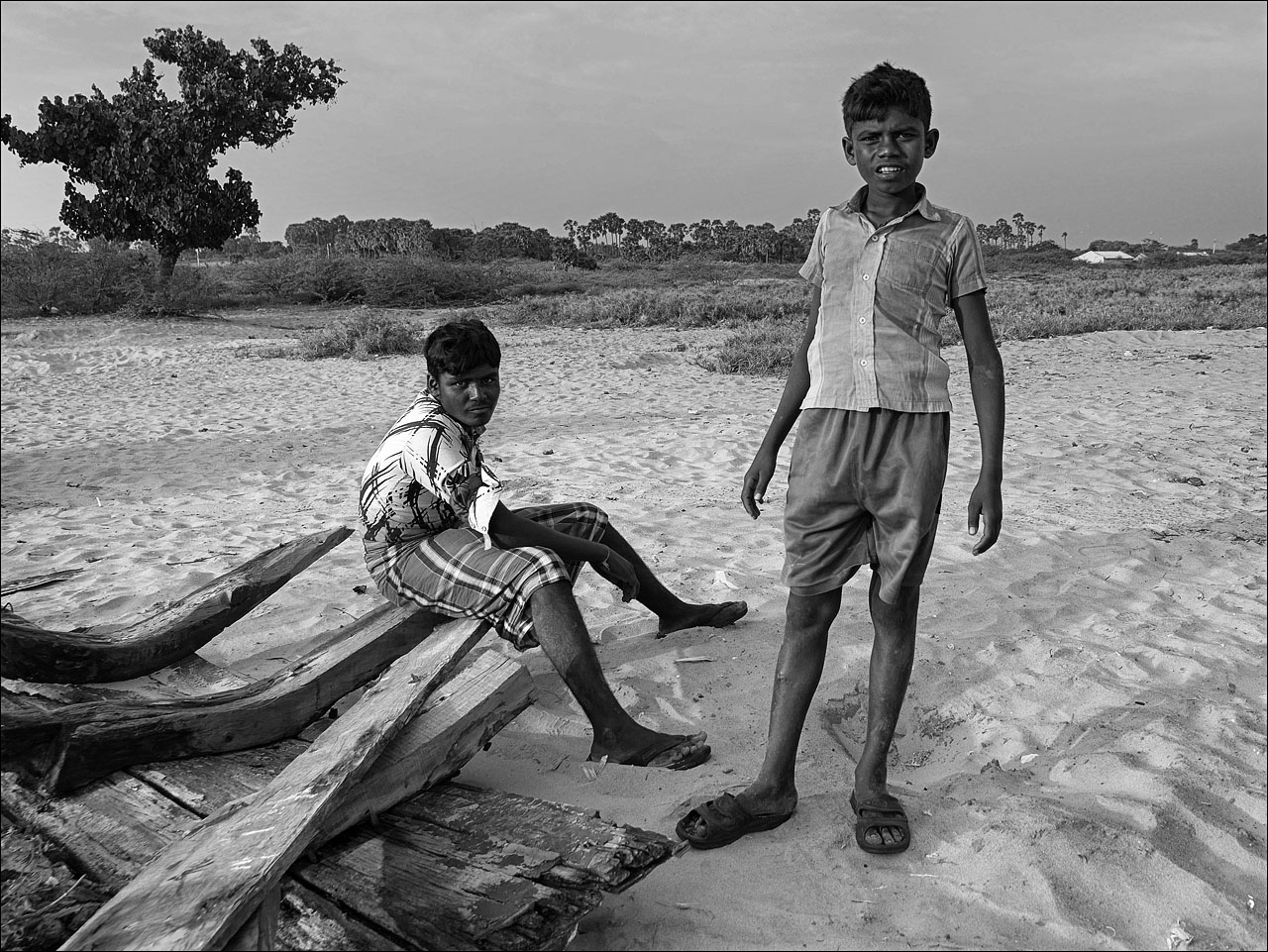 a boy standing next to another person sitting on a bench