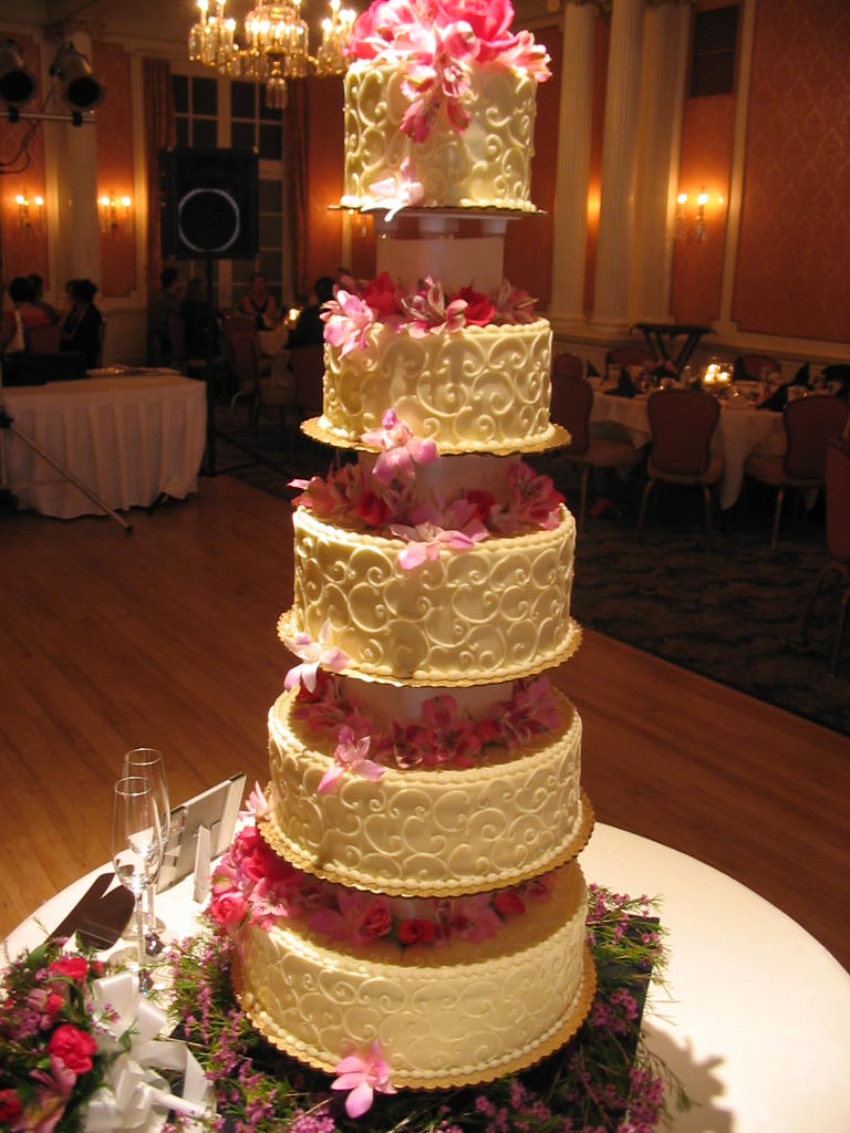 a three layer cake decorated with pink flowers and lace on a table