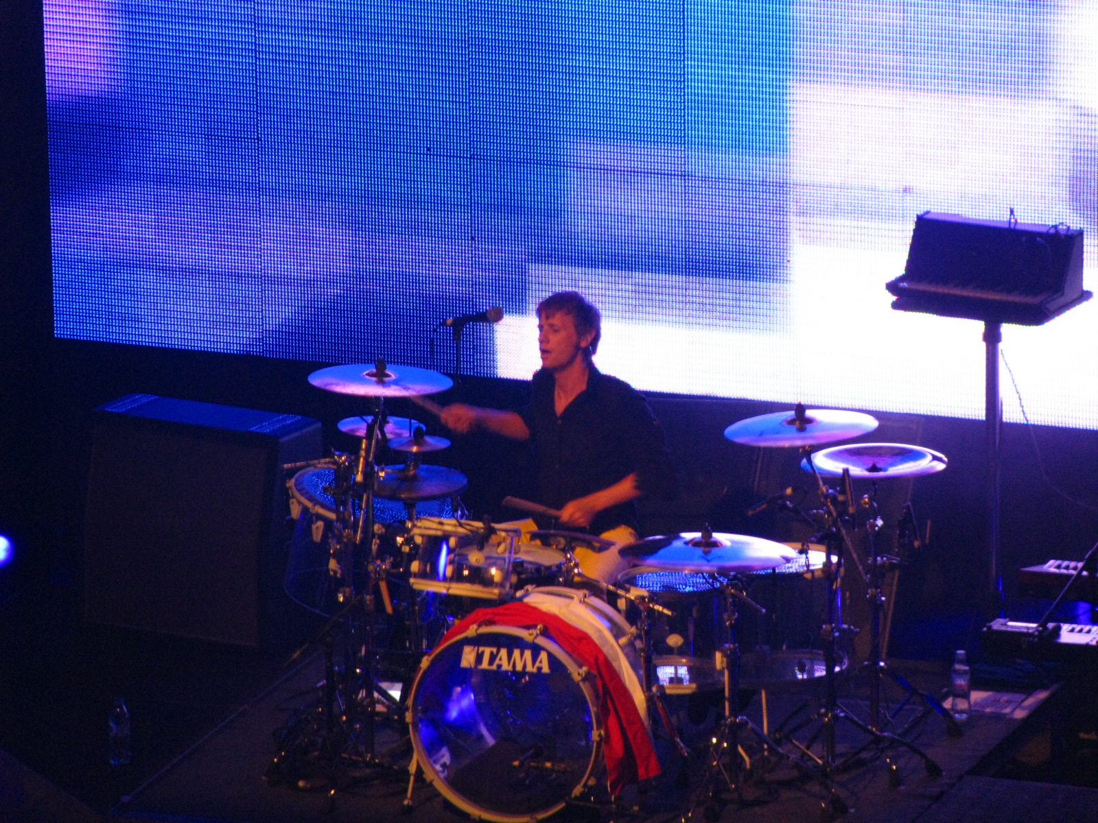 an artistic drummer plays his drums in front of a large screen