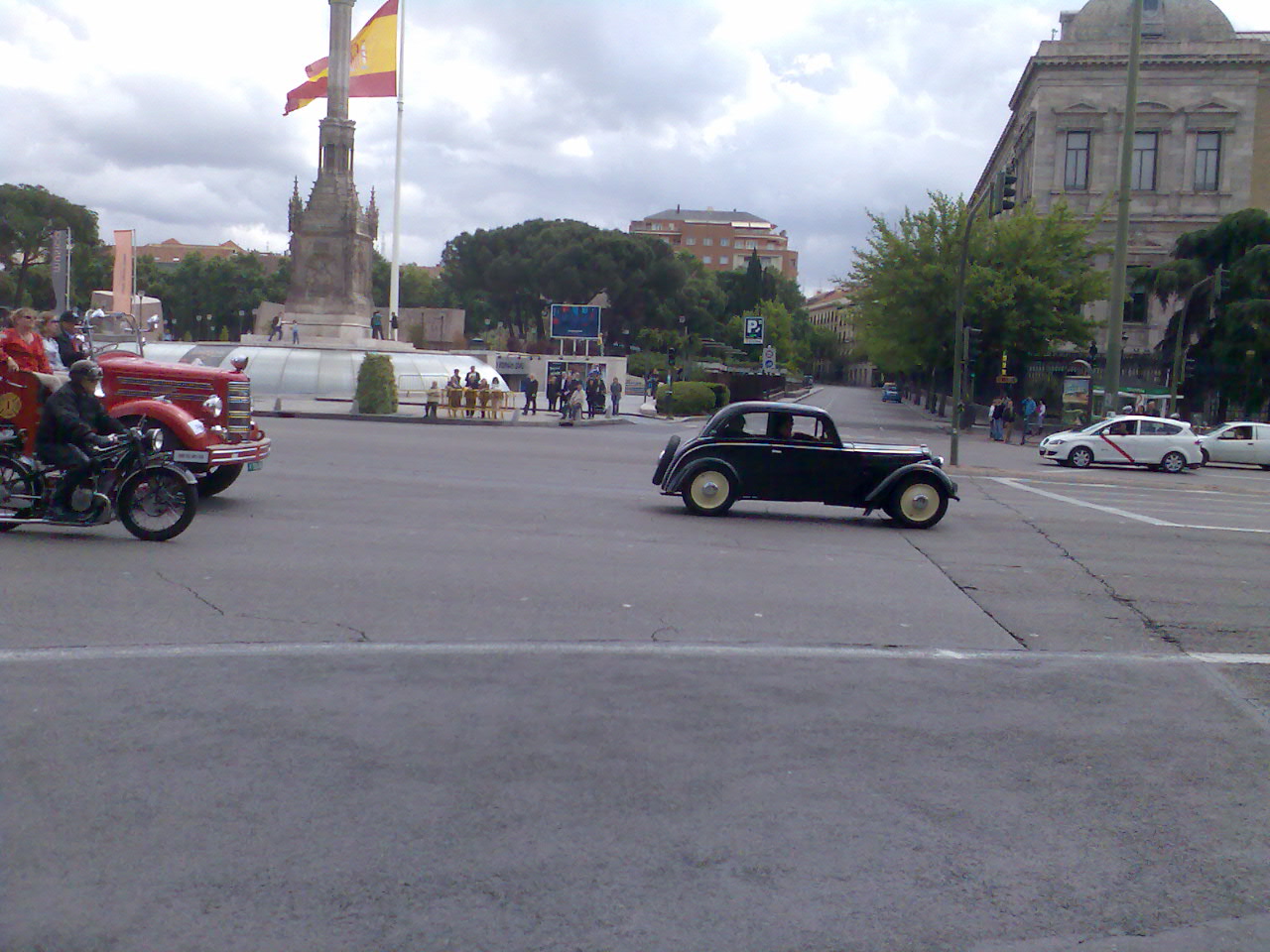 a car and motorcycle passing by in front of a monument