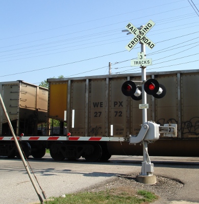 an intersection with a railroad crossing and train cars in the background