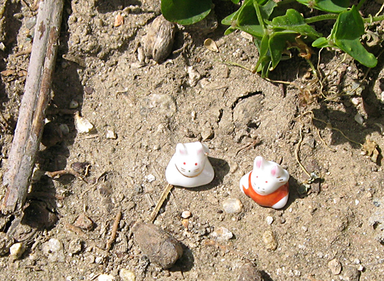 two little white cat figurines on top of dirt