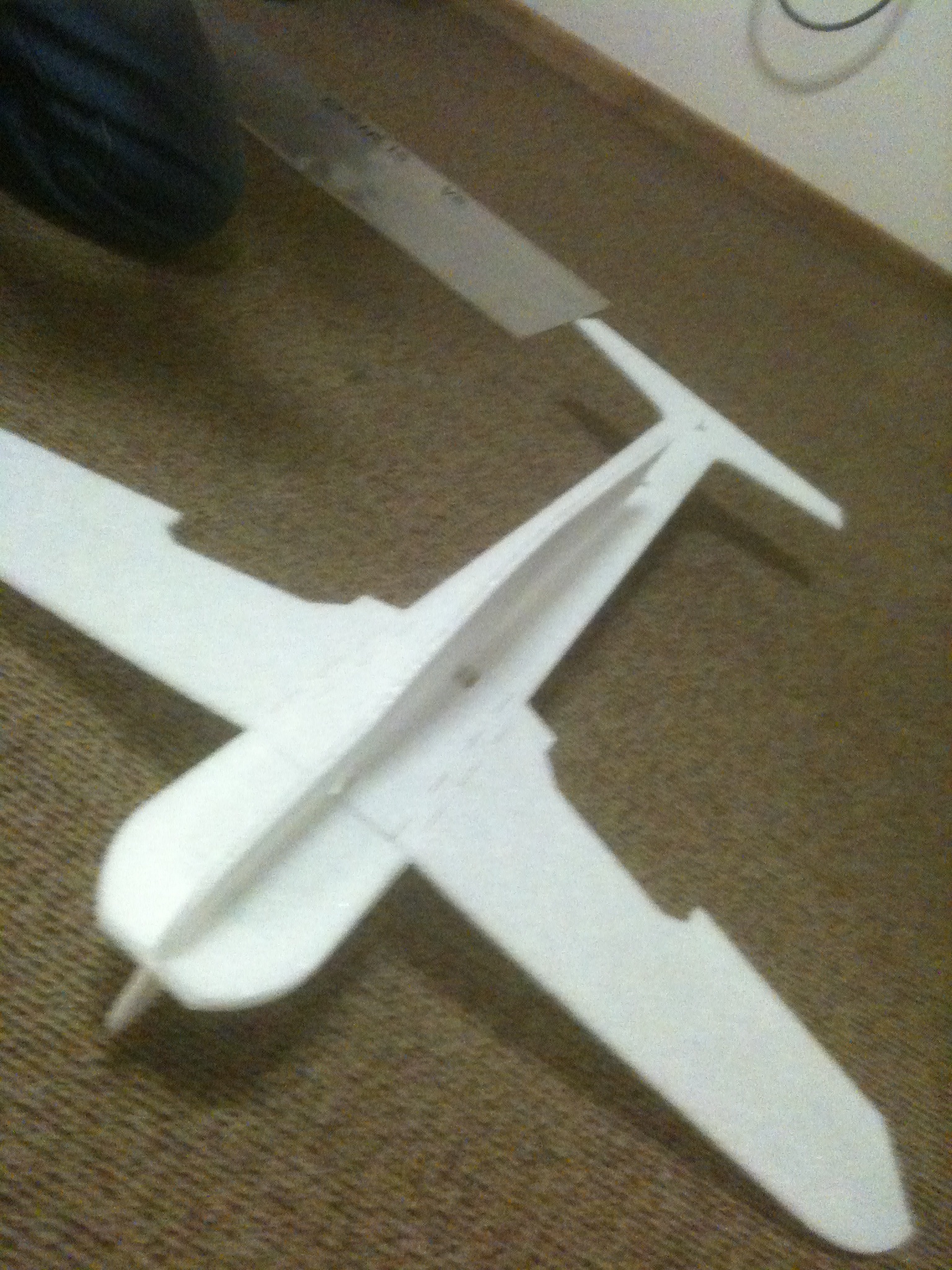 paper airplane model displayed on floor next to large object