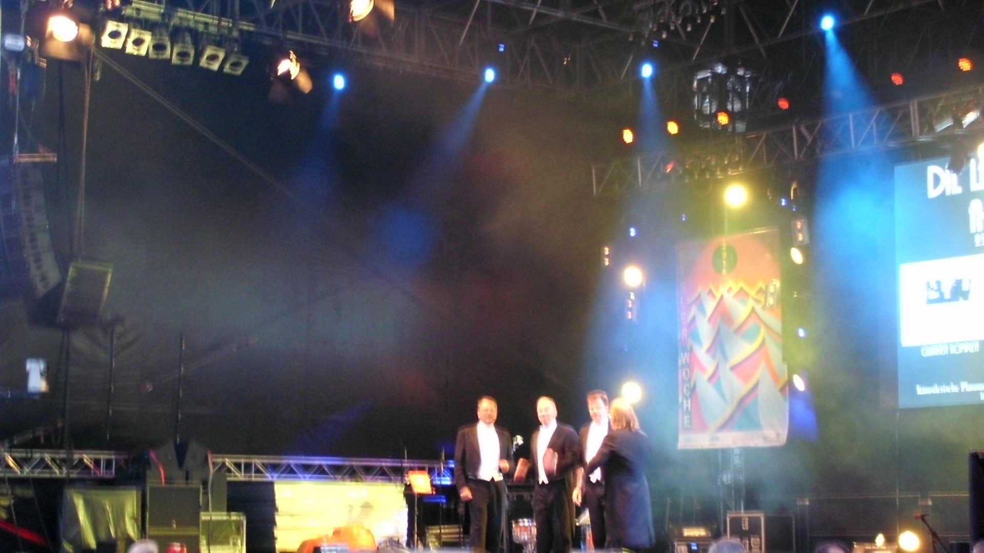three people standing on a stage with their hands in their pockets