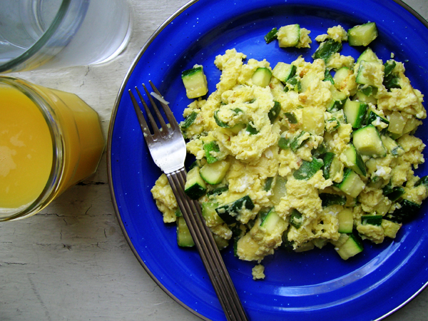 a plate full of scrambled egg salad next to a fork and glass of orange juice