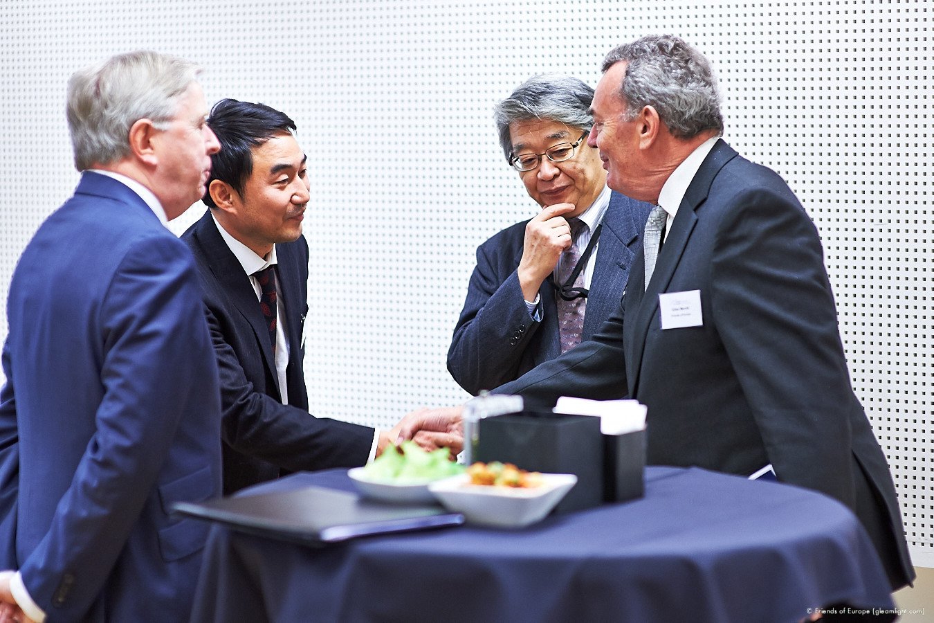 five businessmen shaking hands at a table with a plate of food on it