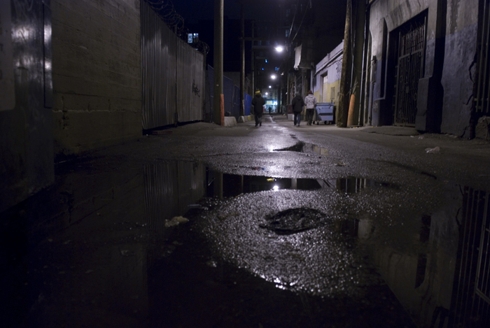 a dark street with a dle of water and a person walking down the sidewalk