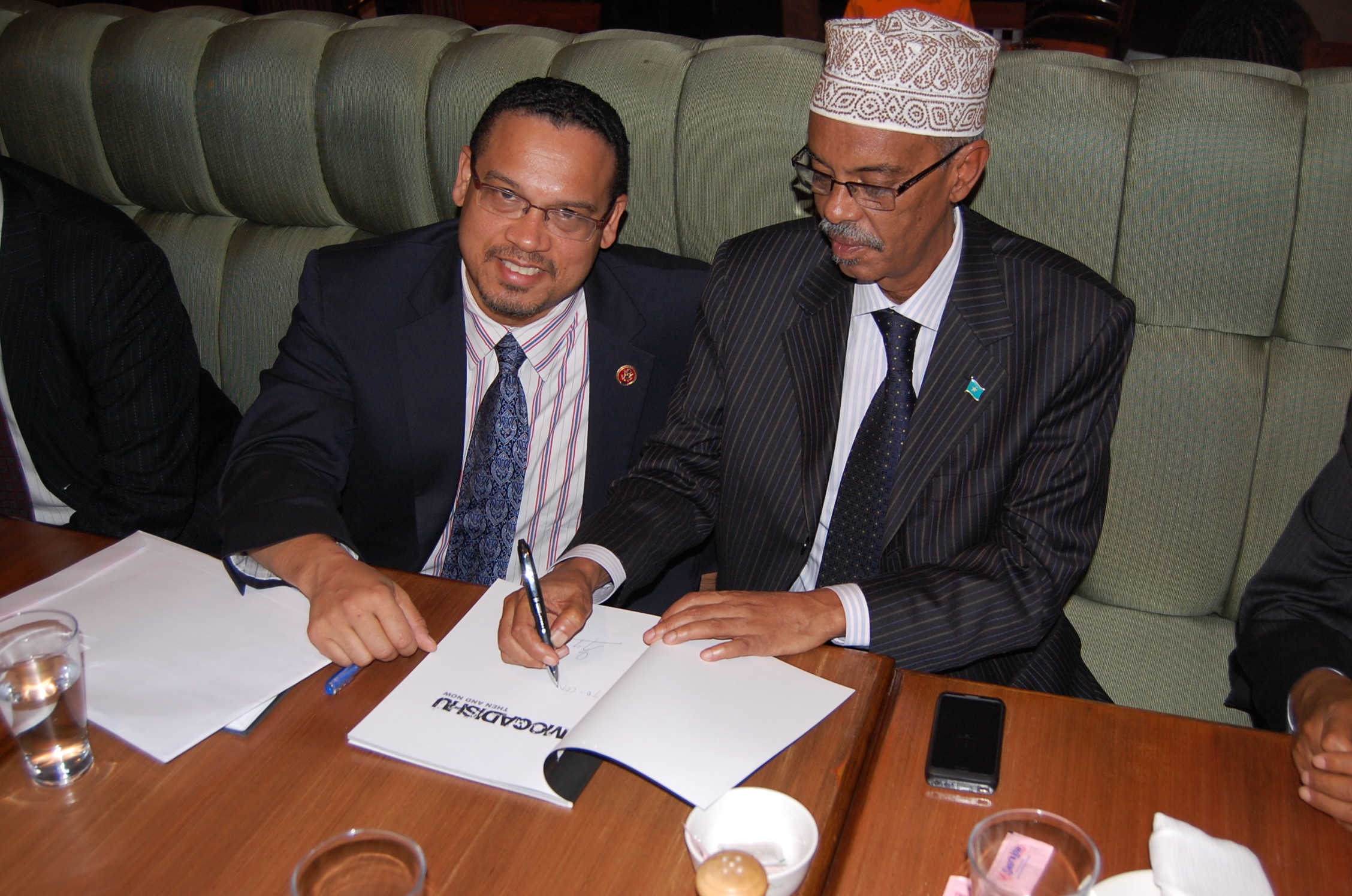 a man sitting next to another man signing papers