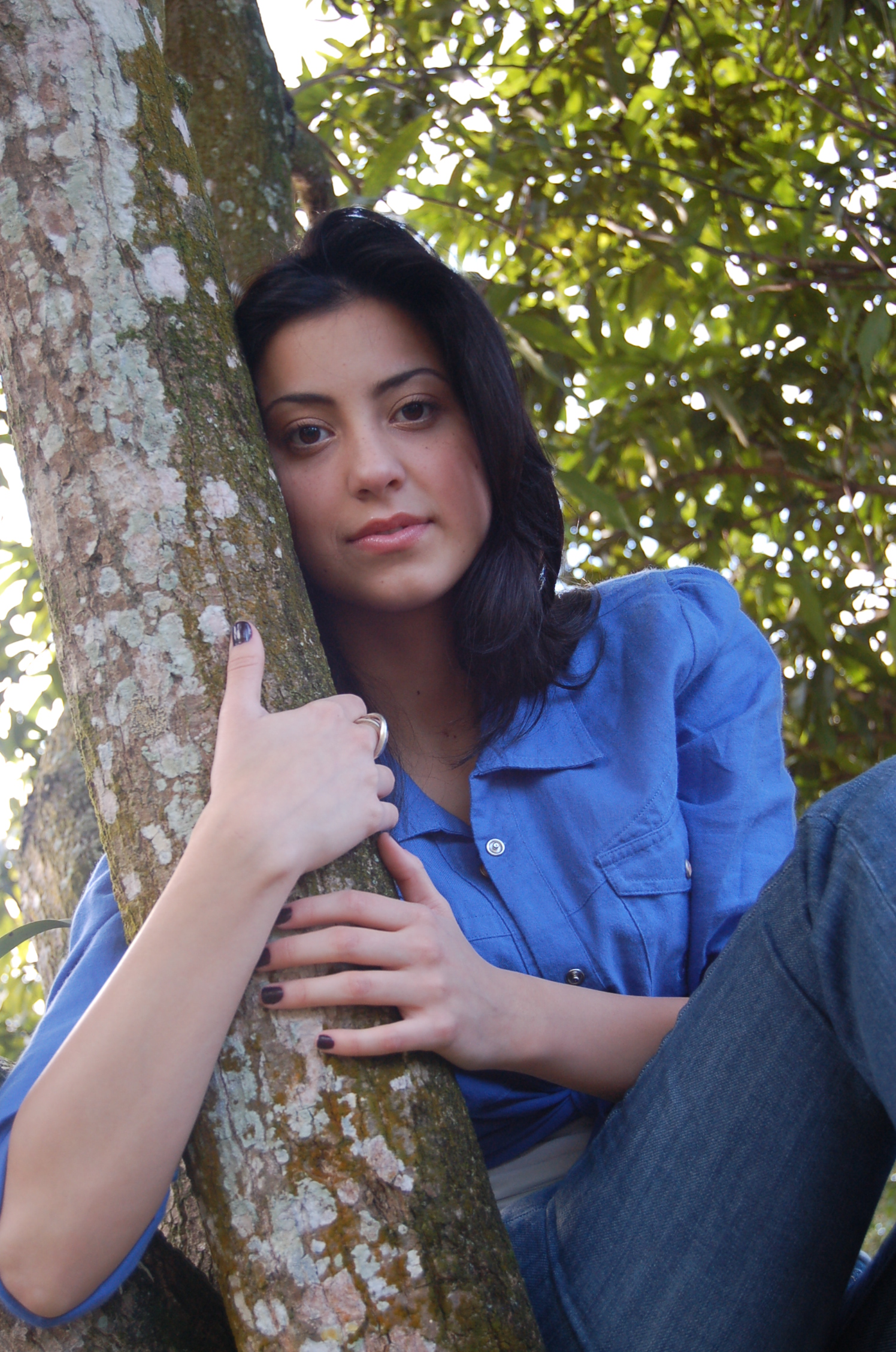 a girl standing up against a tree on her cell phone