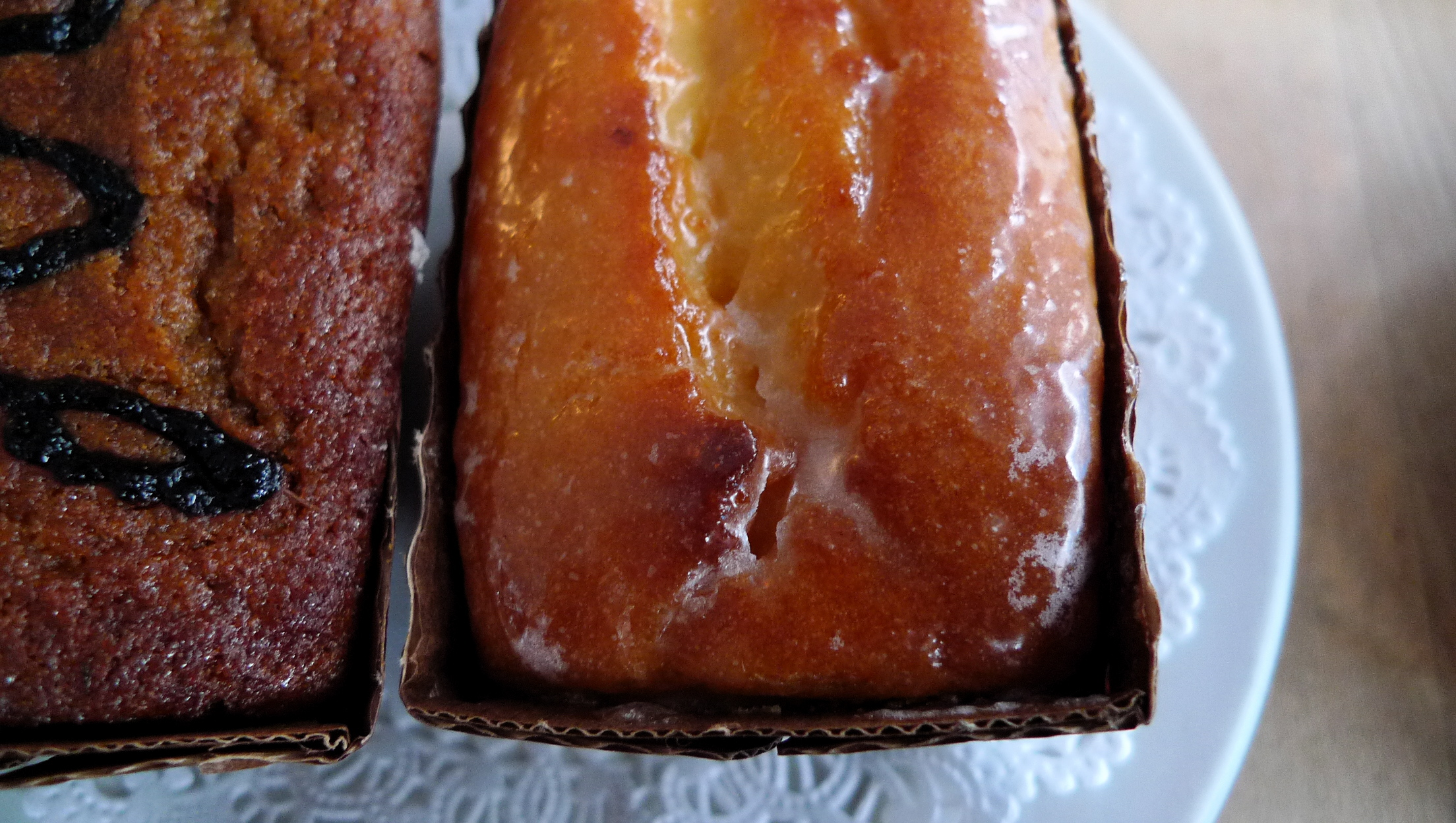 two brown breads on a plate, one has melted icing and the other is fresh fruit