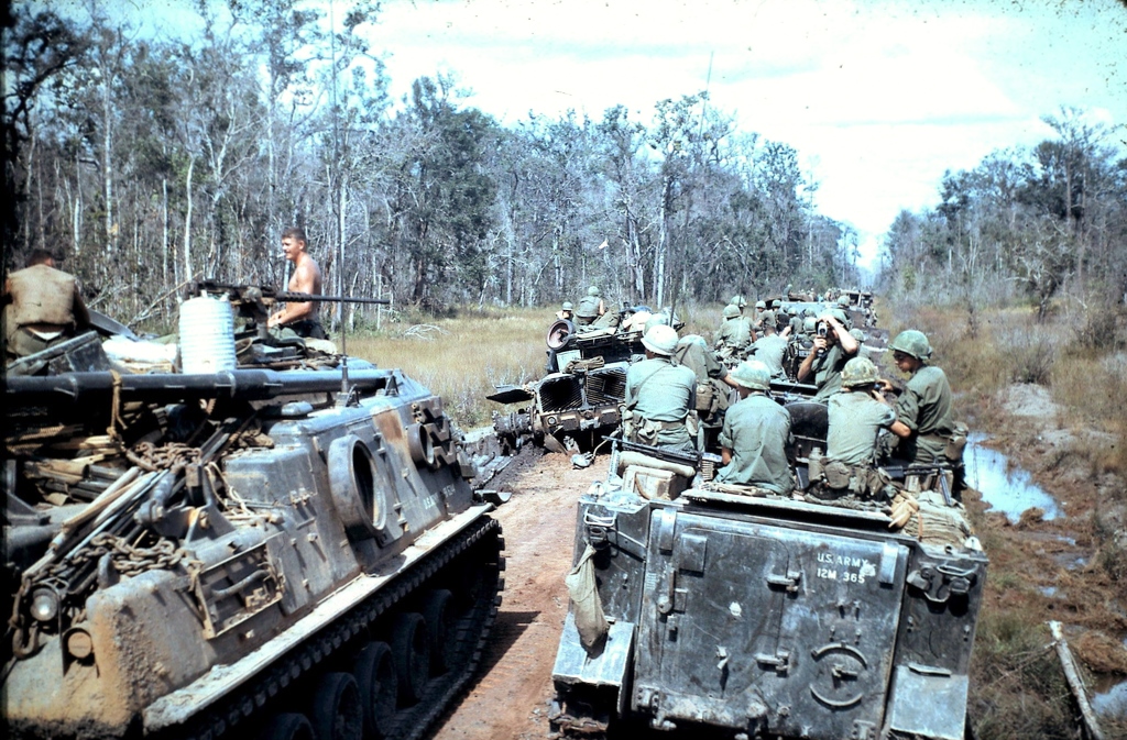 several men and women in tank tops and camouflage coats in the mud