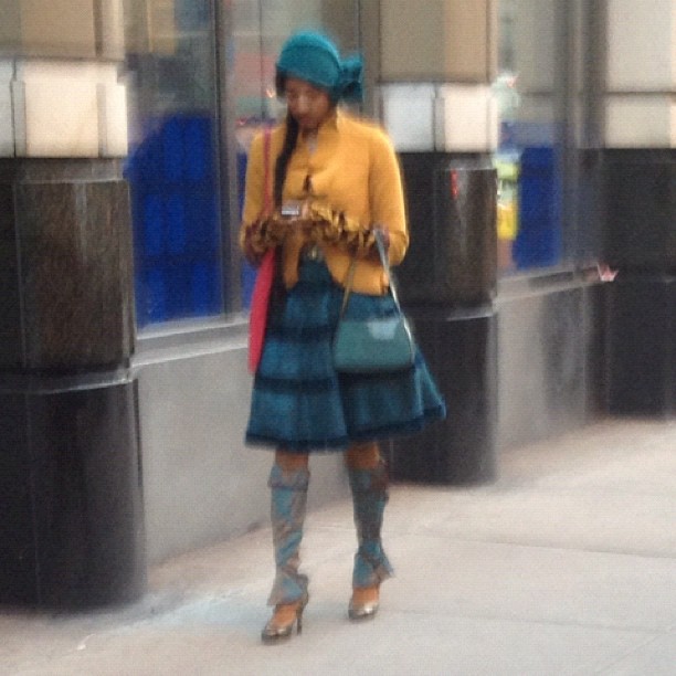 a woman with a hat on and sweater, a green purse and matching boots on