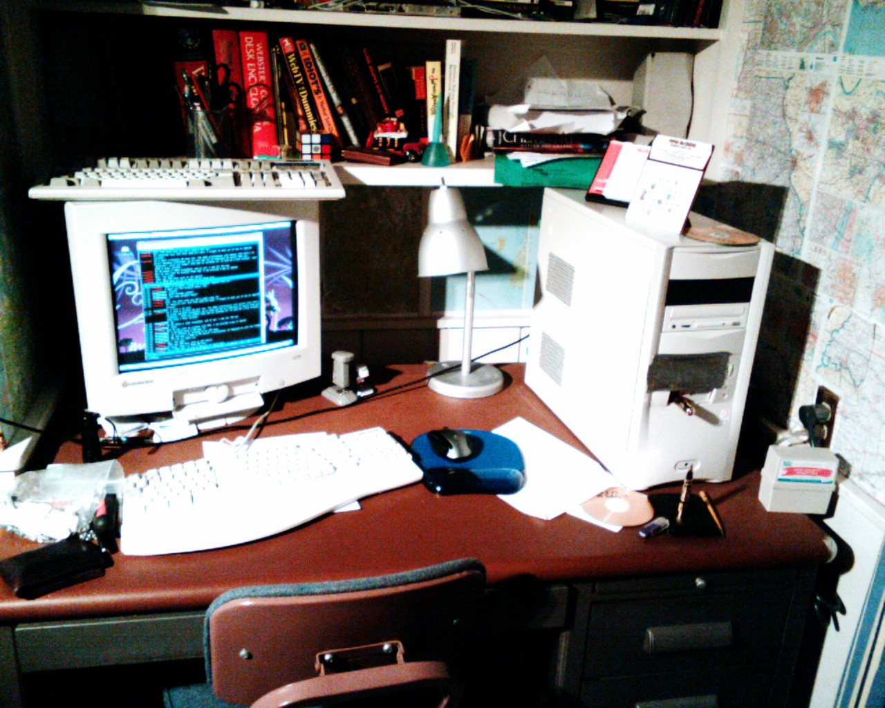a desk has a computer monitor, keyboard, mouse, books and lamp on it