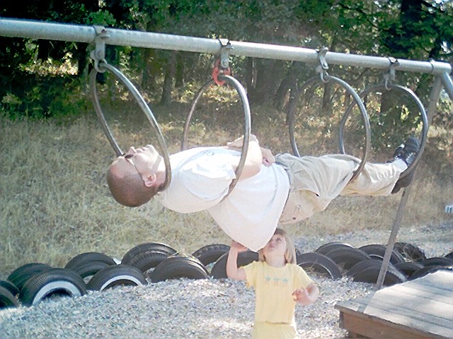 a small child standing in front of a man on a swing