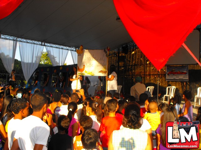 many children sitting under a canopy watching an entertainer stand on stage