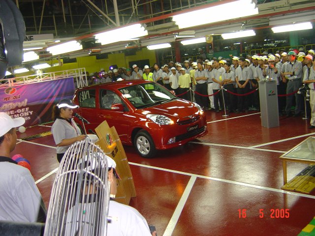 several people standing around an assembly line and two small cars