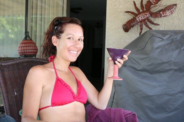 a woman sits in a red bikini and smiles holding a wine glass
