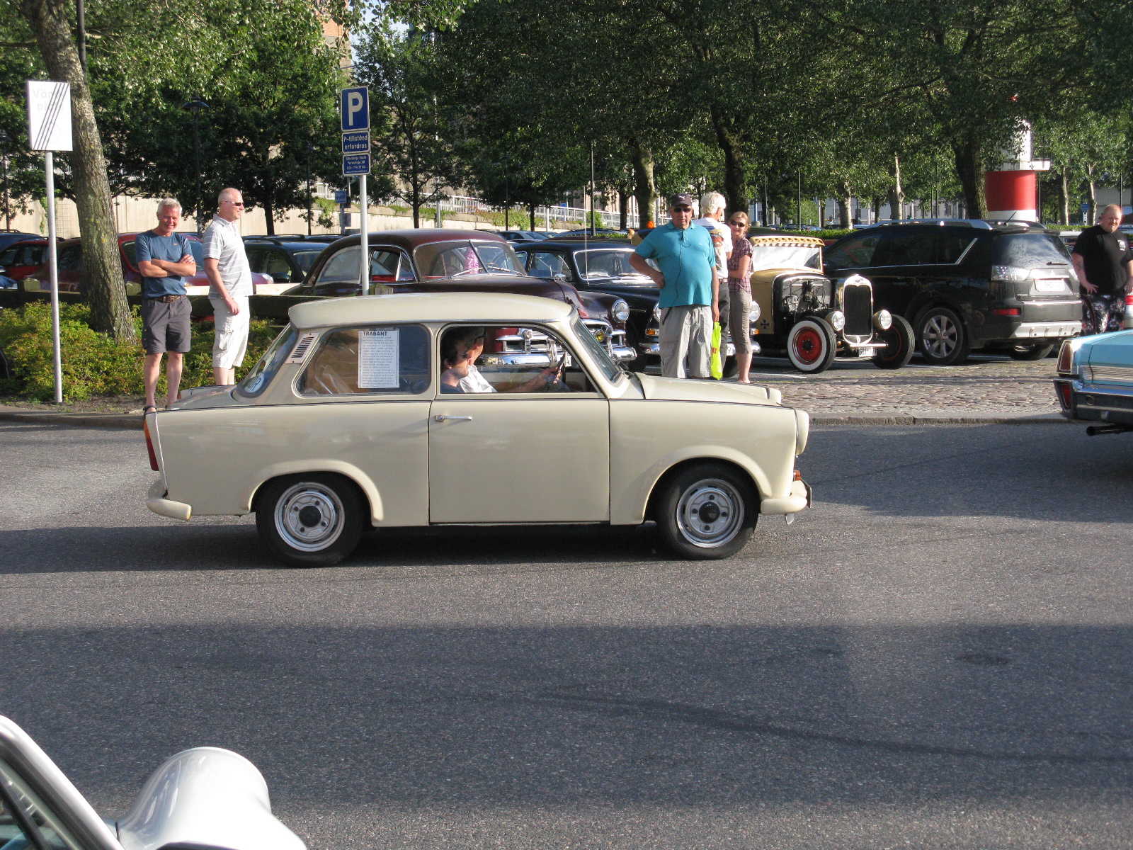 an old car in the middle of a street with people walking