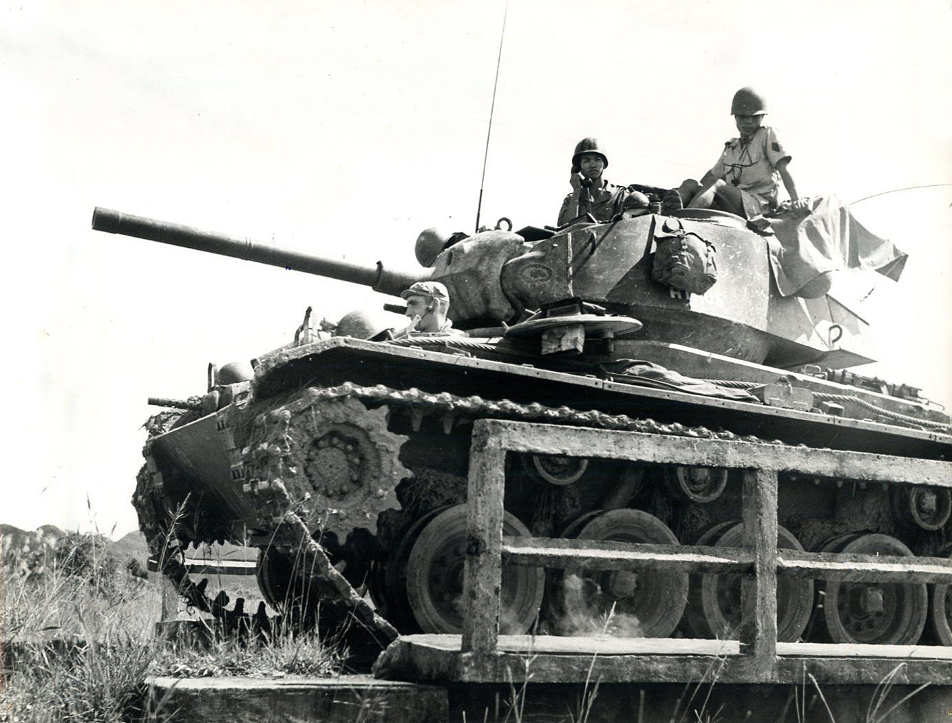 two men riding on top of an army tank