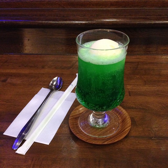 the green cocktail in a wine glass and a spoon are on a table